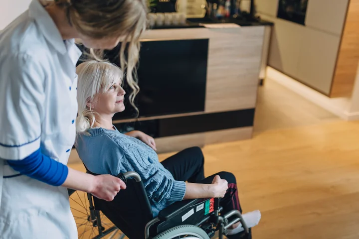 Starsza kobieta na wózku inwalidzkim popychana przez opiekunkę w kuchni