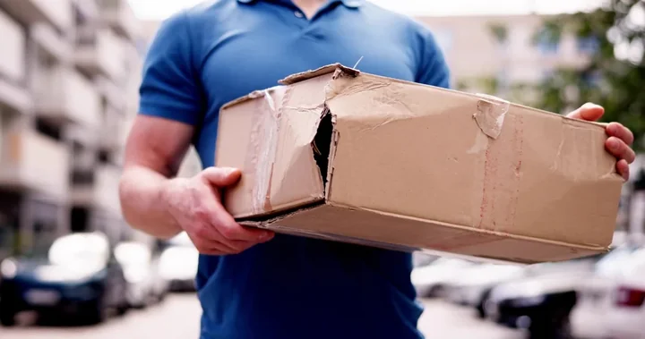 Zdjęcie przedstawia mężczyznę trzymającego uszkodzoną paczkę