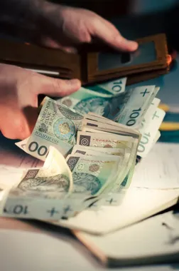 Dłonie wyjmujące i liczące banknoty polskich złotych z portfela.